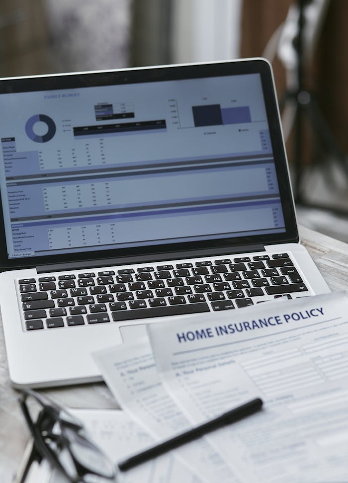 gallery-03 Close-up of home insurance policy papers with a laptop displaying financial analysis.